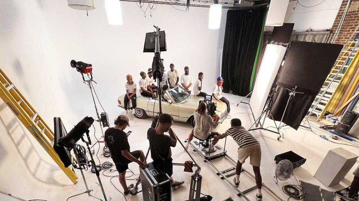 A large film studio space where a dolly and track is setup with artist sitting on top of a car for music video shoot
